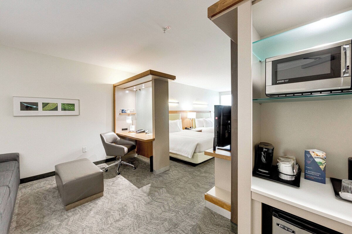 A hotel room with a bed, a desk, a chair, a microwave, and a coffee maker.