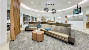 A modern lobby with a curved ceiling, a sectional sofa, a round coffee table, and a TV mounted on the wall.
