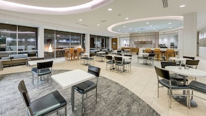 A spacious indoor dining area with multiple tables and chairs, large windows, and a modern ceiling design.