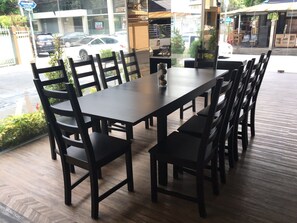 A dining area with a long table and multiple chairs, a vase with flowers, and a view of the street outside. - Tonaor Place Bangkok (Bangkok)