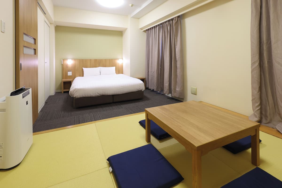 A hotel room with a bed, a wooden table, and a futon.