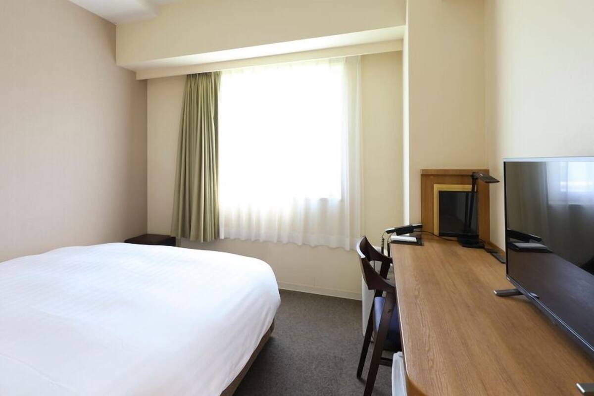 A hotel room with a bed, a desk, a chair, a television, and a window with curtains.