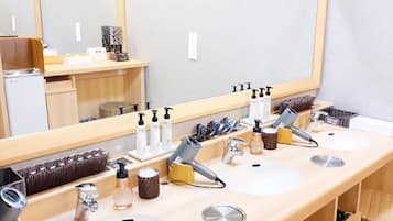 Un baño con tres lavamanos, un espejo grande y distintos artículos de aseo.