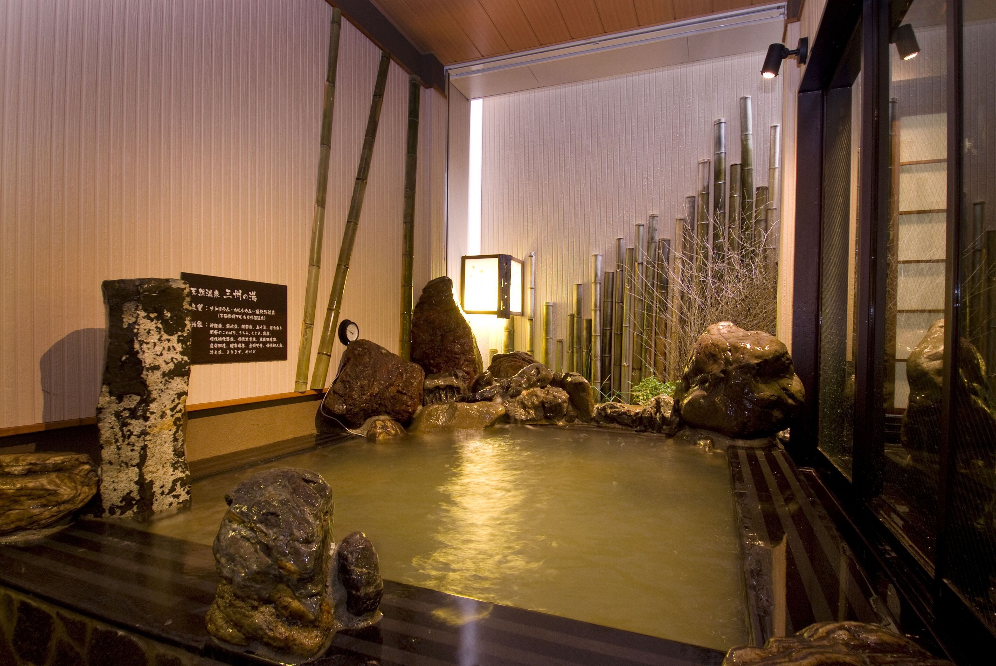 A traditional Japanese onsen with a rock garden, bamboo, and a wooden bath area.