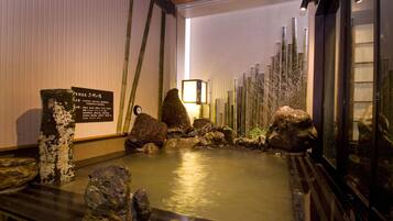 A traditional Japanese onsen with a rock garden, bamboo, and a wooden bath area.