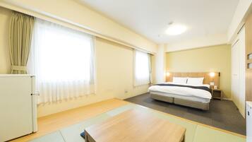 Habitación de hotel pequeña con una cama individual, una mesita, un refrigerador y una ventana con cortinas.