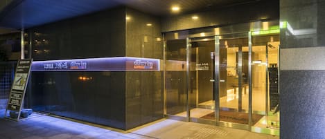 A hotel entrance with a glass door, a signboard, and a tiled floor.