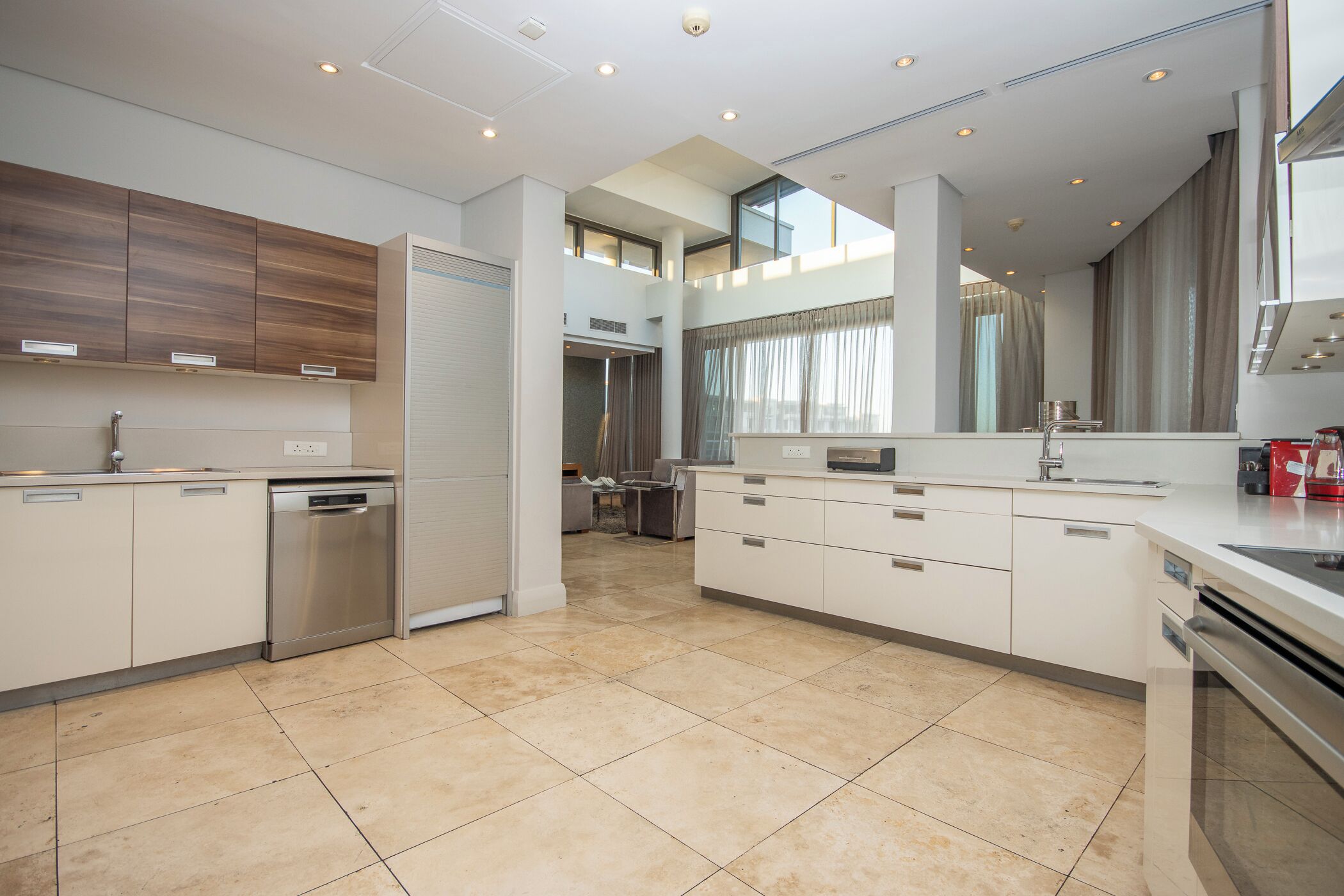 A modern kitchen with a dishwasher, double sink, and a dining area with a chair.