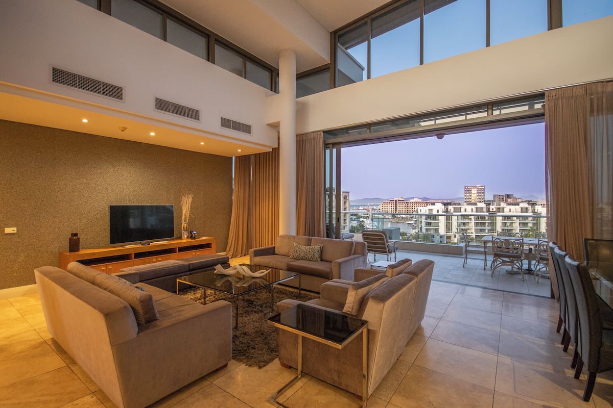 Een moderne woonkamer met een flatscreen televisie, banken, een salontafel en een balkon met uitzicht op de stad.