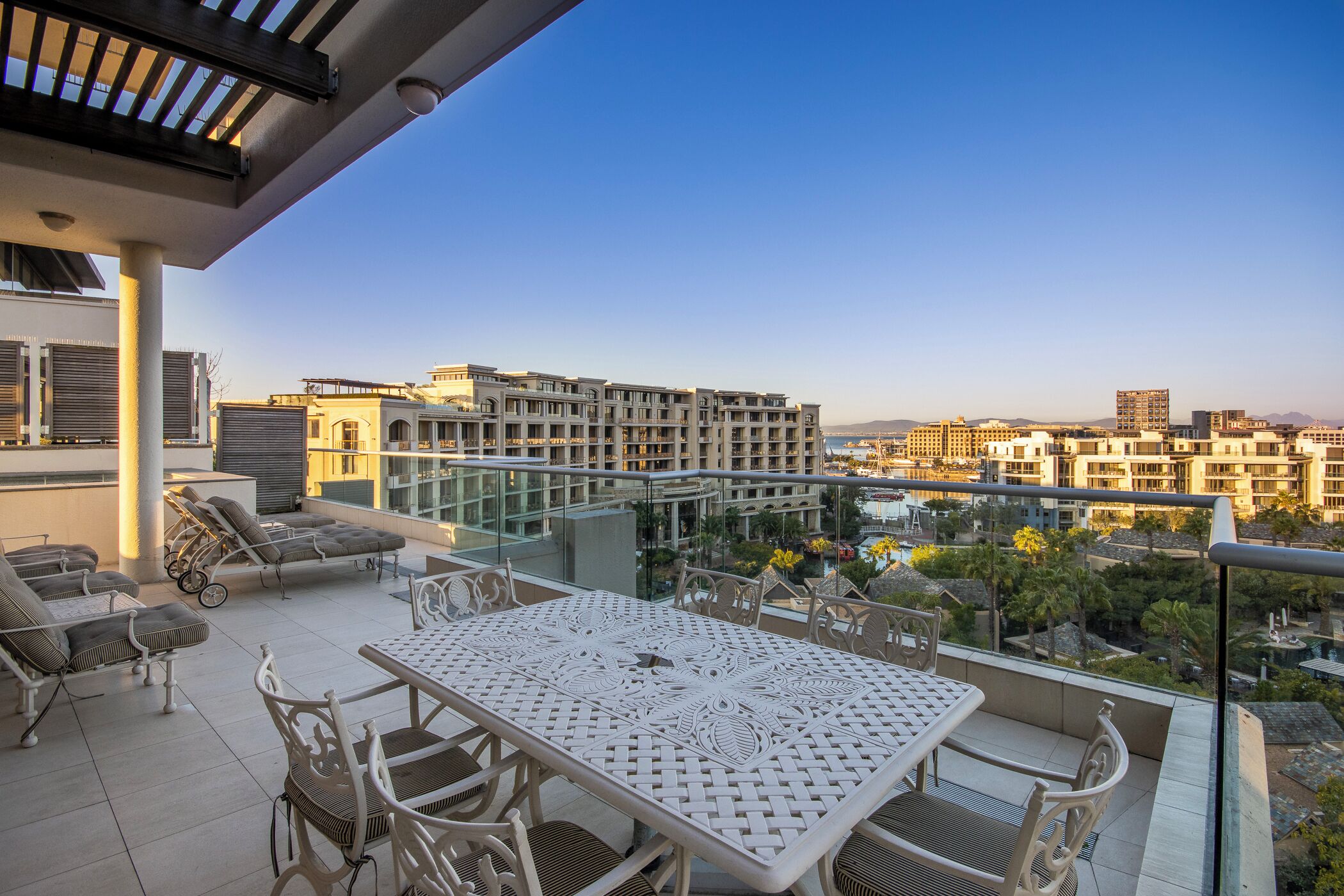 A balcony with a table and chairs, overlooking a cityscape with modern buildings.