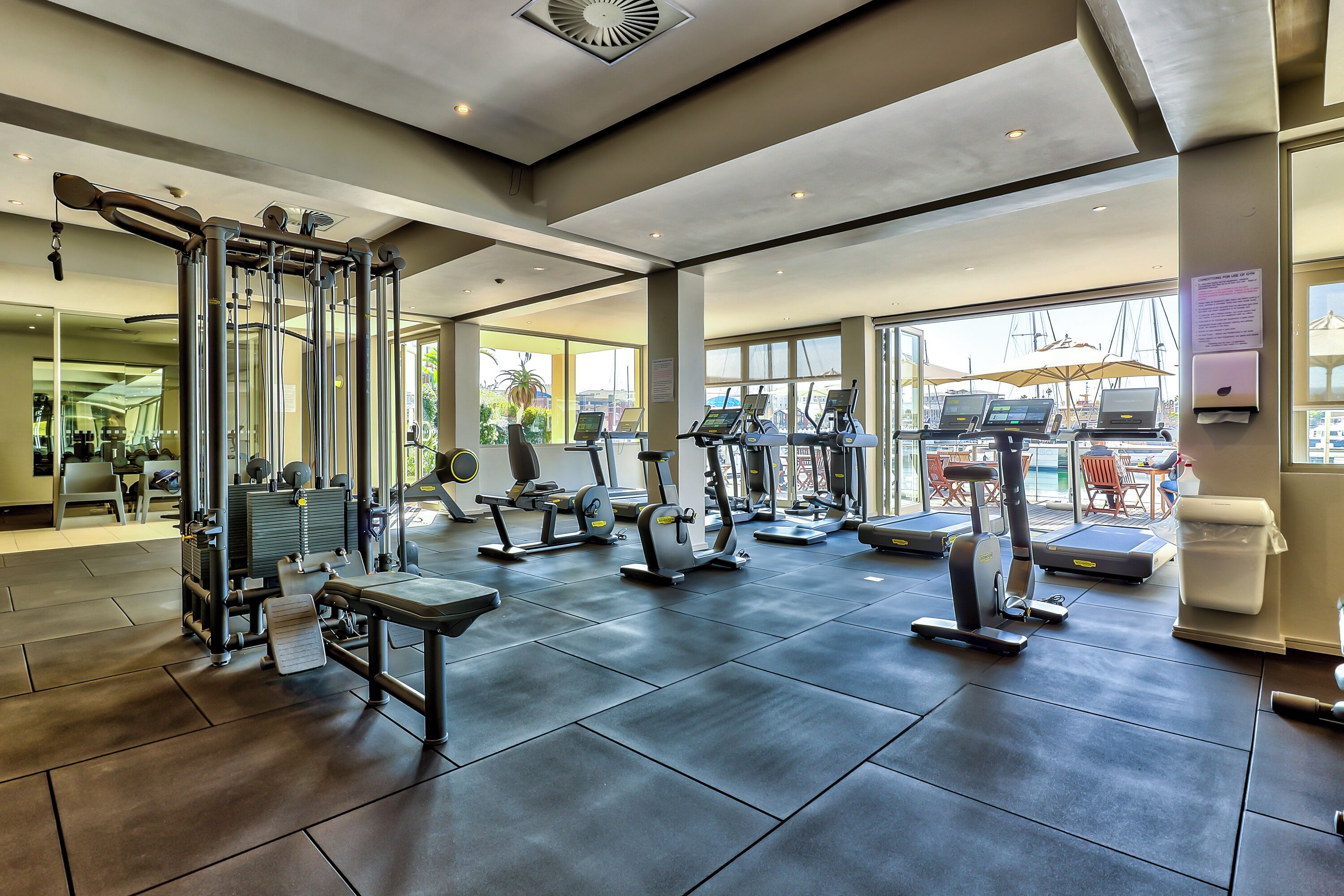 A gym with various exercise equipment, large windows, and a view of the outside.