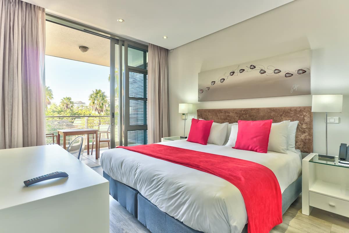 Een moderne hotelkamer met een groot bed, een bureau en een balkon met uitzicht op palmbomen.