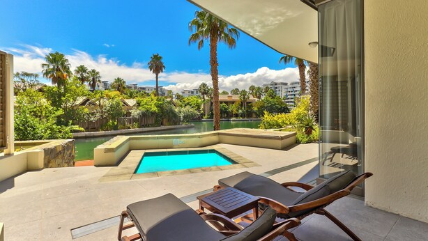 Zona junto a la piscina con sillones de descanso y una mesa, con vistas a una piscina y abundante vegetación.