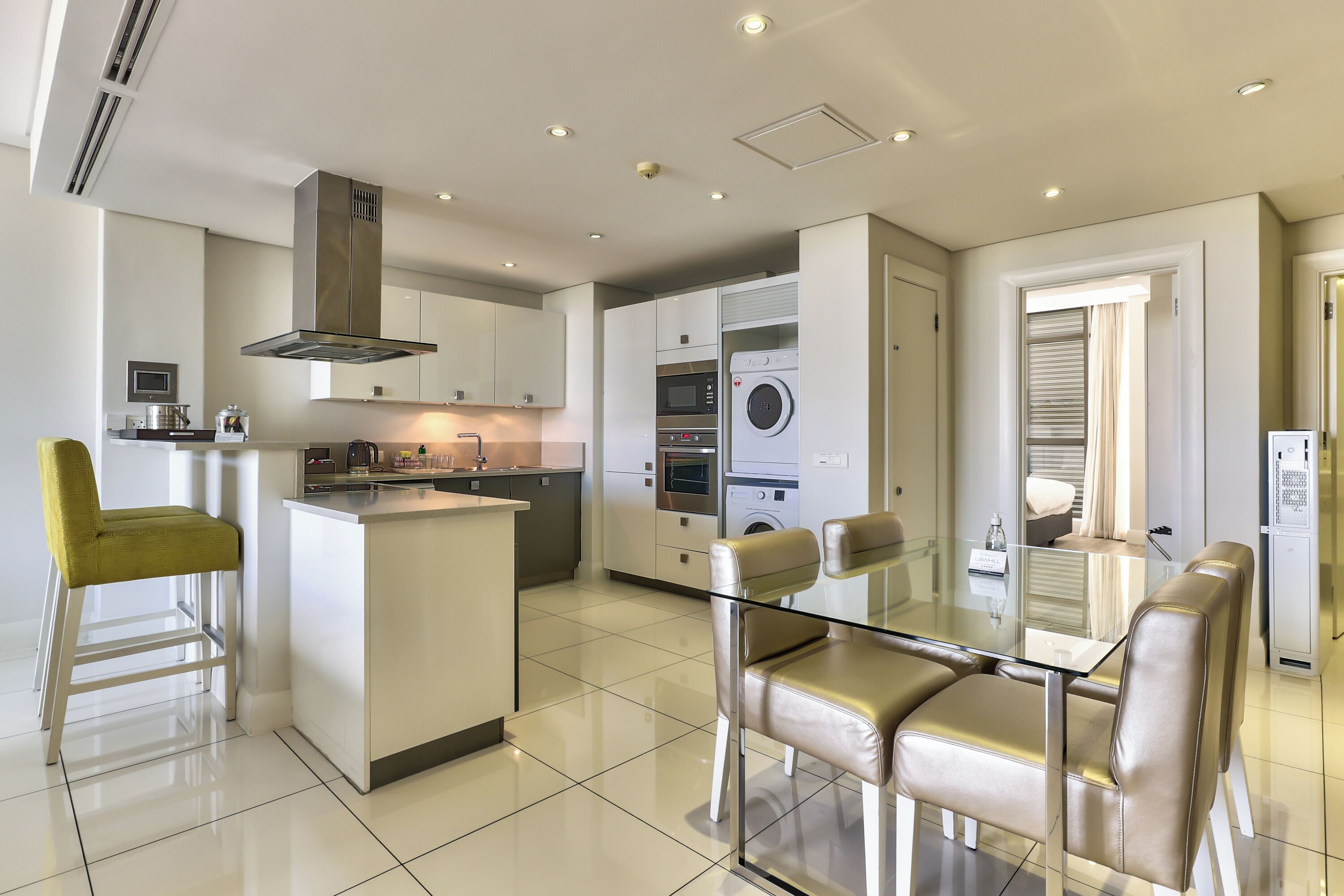 A modern kitchen with a central island, built-in appliances, and a dining area with glass-top table and leather chairs.