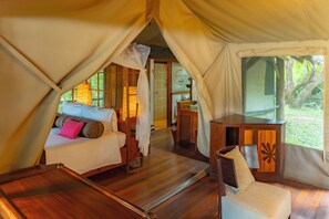 A tented accommodation with a bed, a wooden table, and a view of the outdoors.