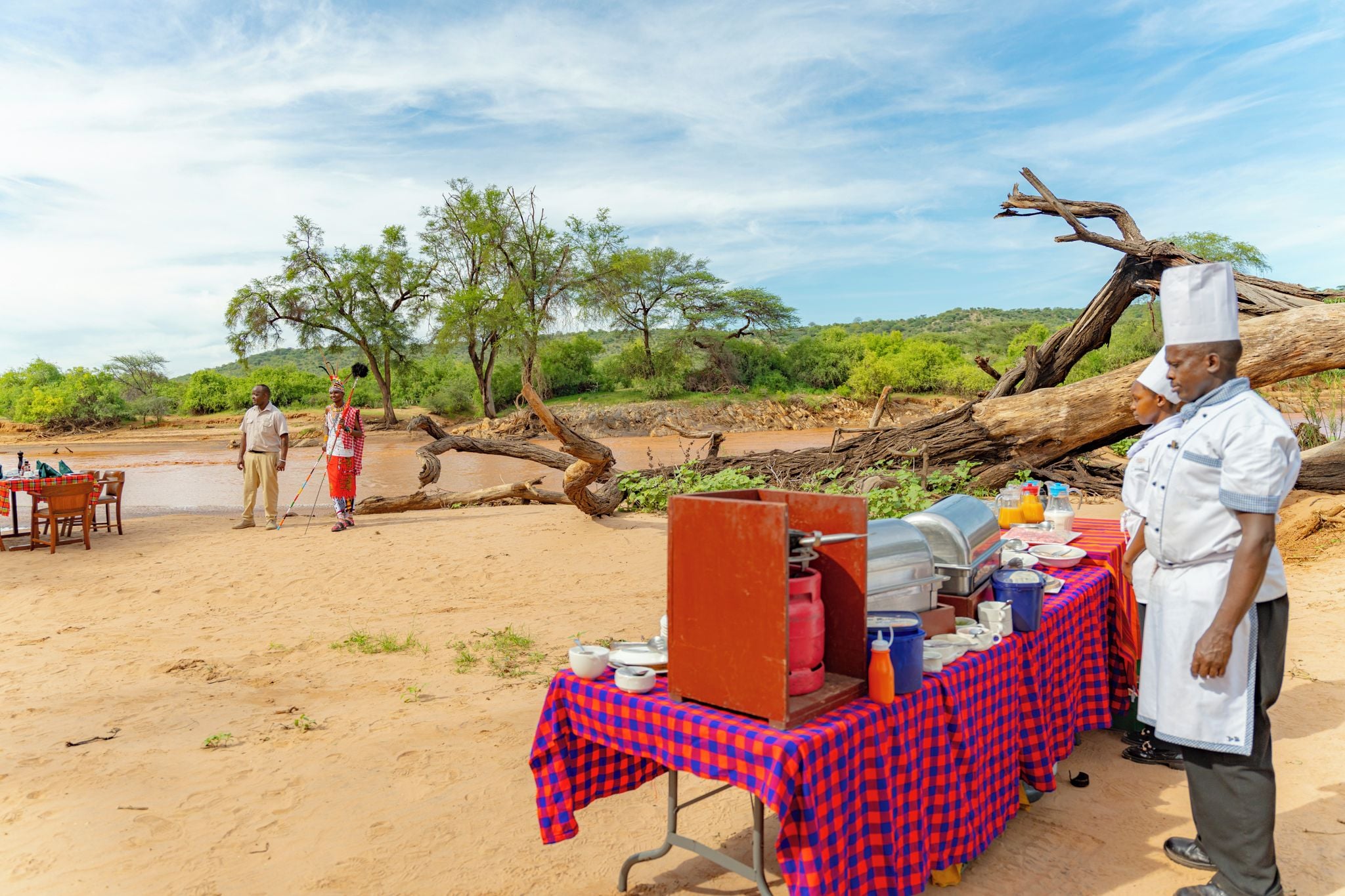 Een buitenterras met een buffetopstelling, een omgevallen boom en een persoon in traditionele kleding.