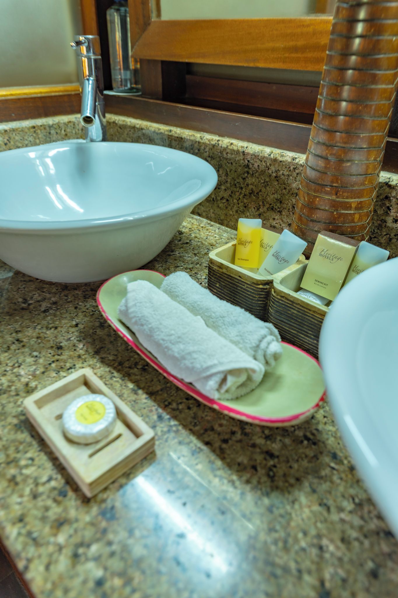 A bathroom sink, a towel, a soap dish, and toiletries on a granite countertop.