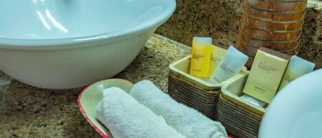 A bathroom sink, a towel, a soap dish, and toiletries on a granite countertop.