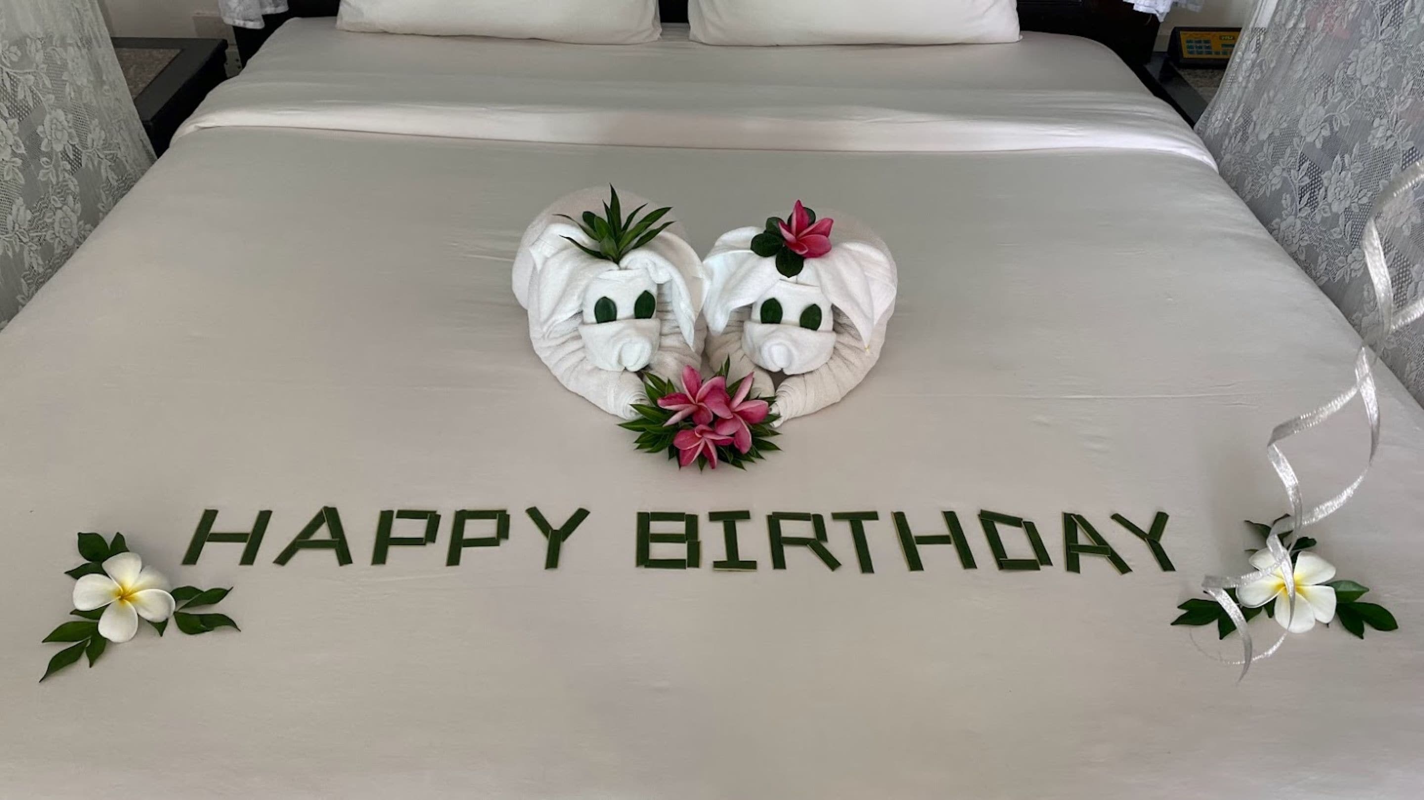 A bed with a white bedspread, two towels shaped like elephants, and a 'Happy Birthday' message.