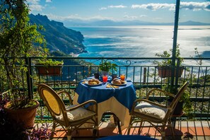 A terrace with a table set for breakfast overlooking a coastal view.