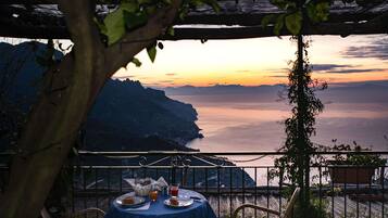 A table set for two with a view of the sea and mountains at sunset.