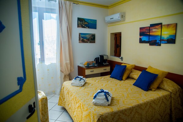 A hotel room with a bed, a desk, a chair, a window with curtains, and artwork on the walls.