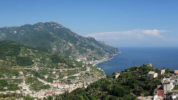 A coastal town with mountainous terrain in the background, a clear view of the sea, and a mix of residential and possibly historical buildings.
