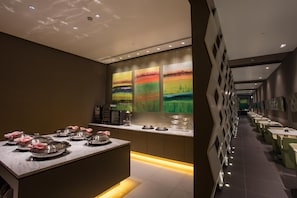 A modern dining area with a long counter, multiple tables, and a central island with covered dishes.