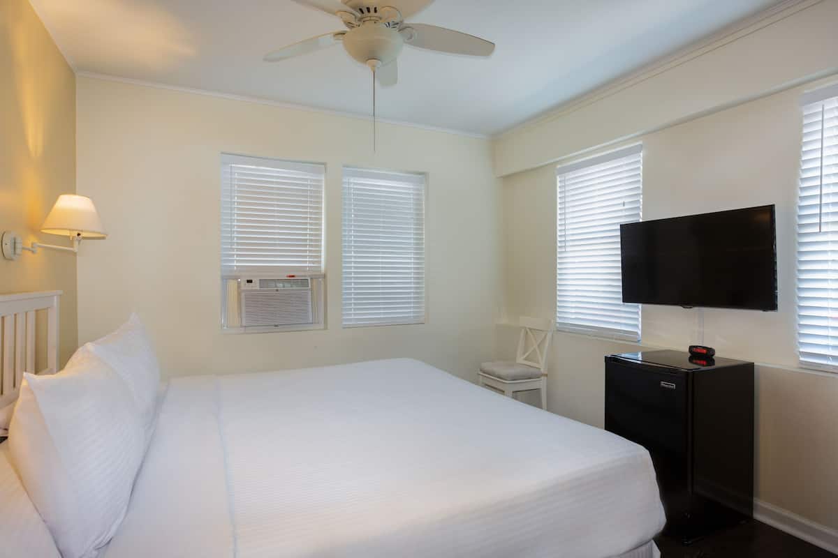 A hotel room with a bed, a desk, a TV, and a ceiling fan.