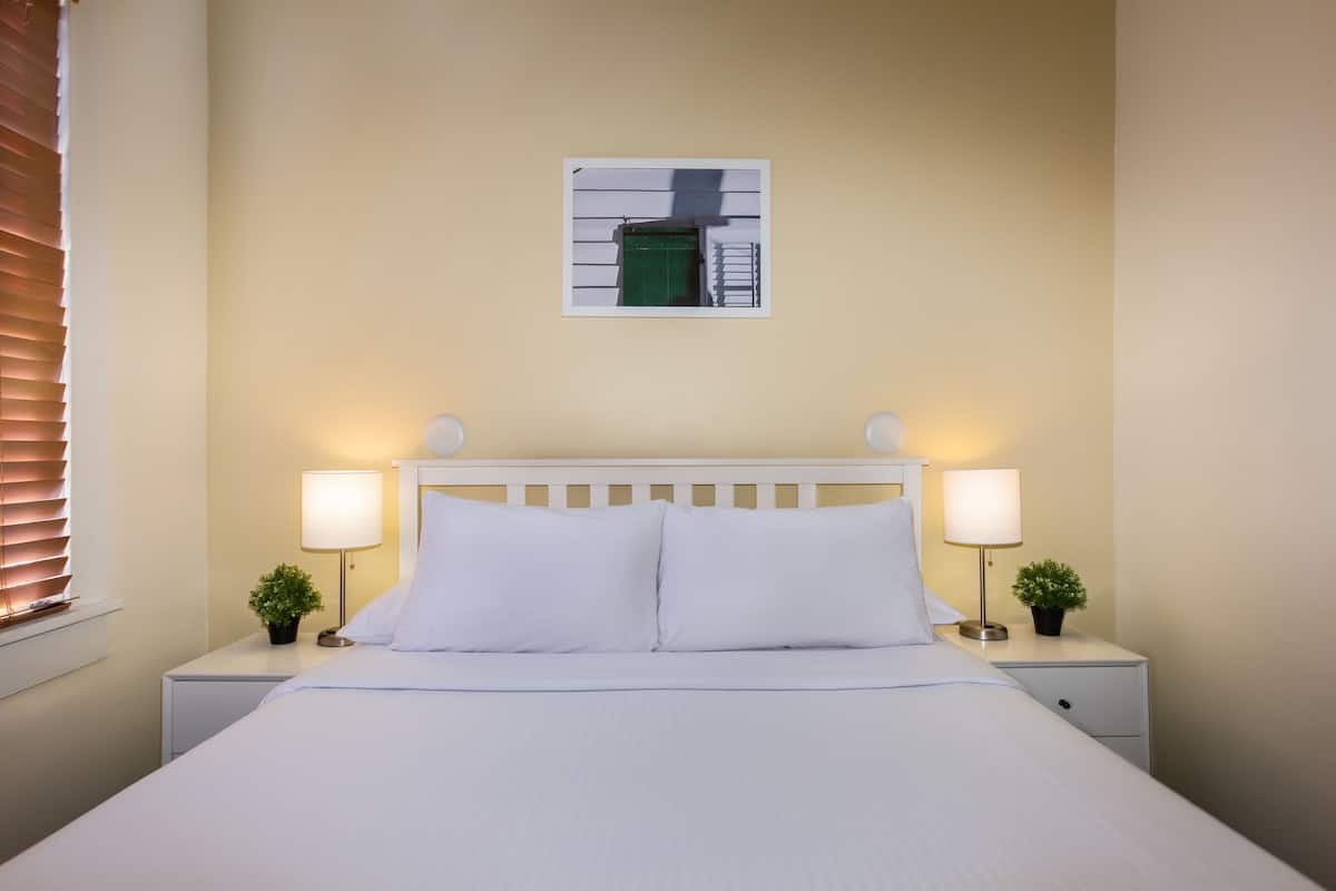 A neatly made bed with white linens, two bedside lamps, and a small plant on each nightstand.