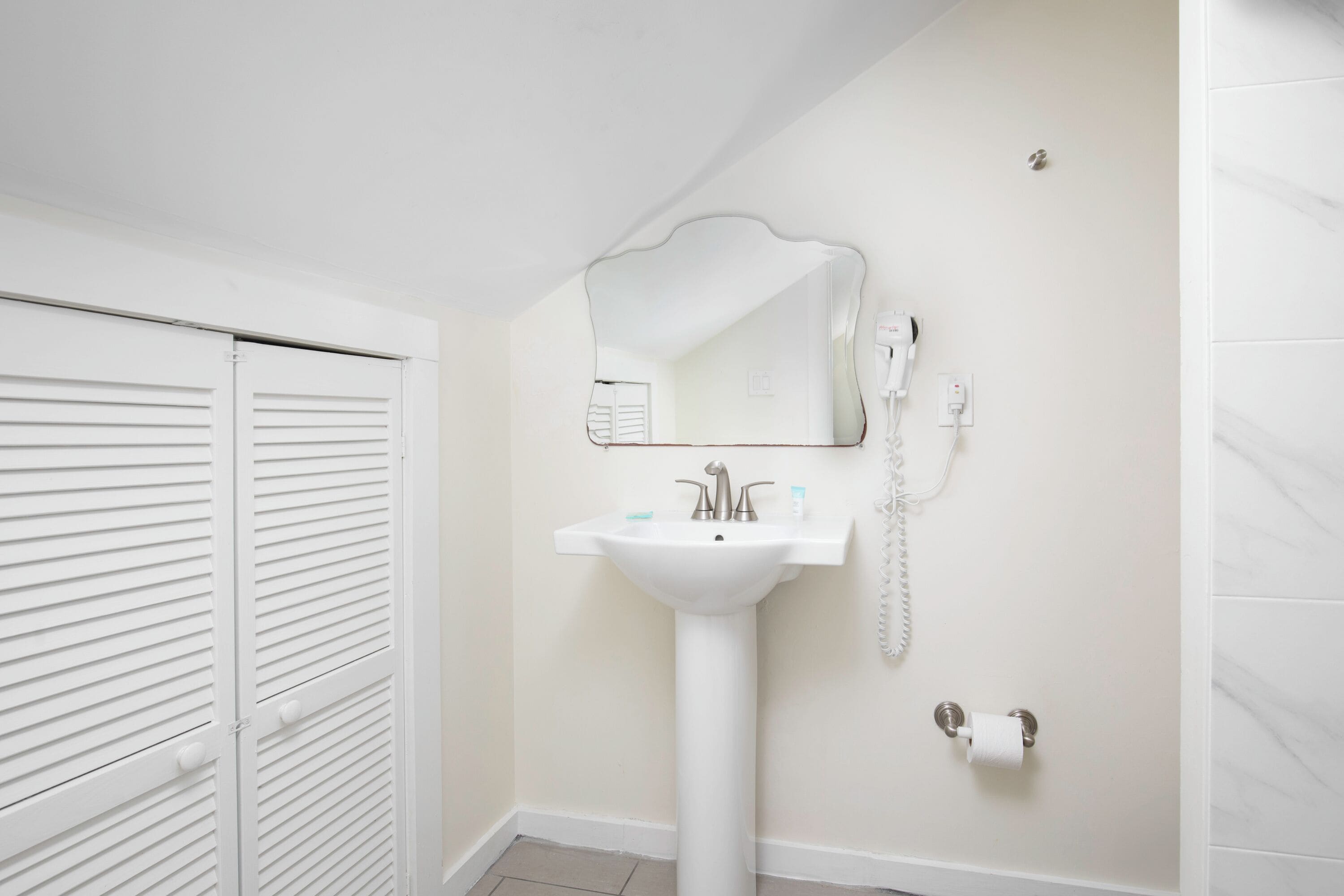 A bathroom with a white sink, a mirror, a telephone, and a toilet paper holder.