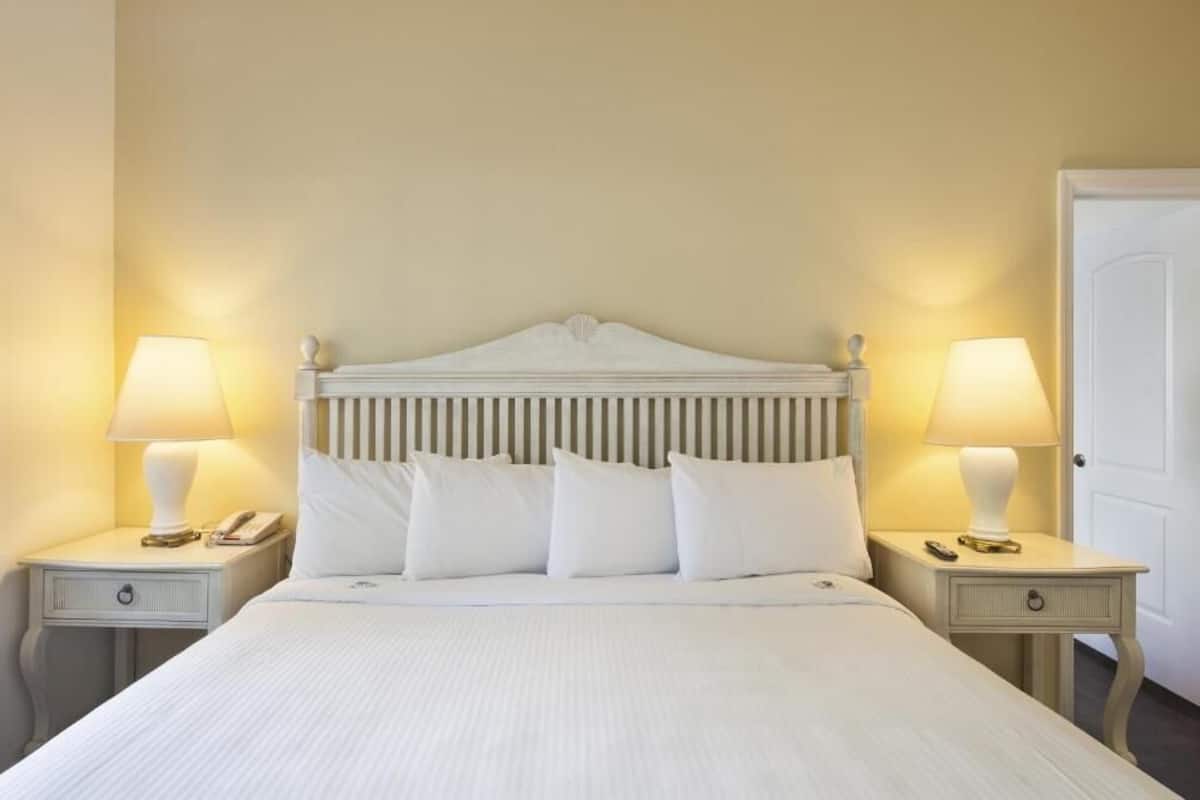 A neatly made bed with white linens and a headboard with vertical slats. There are two bedside tables, each with a lamp and a phone.