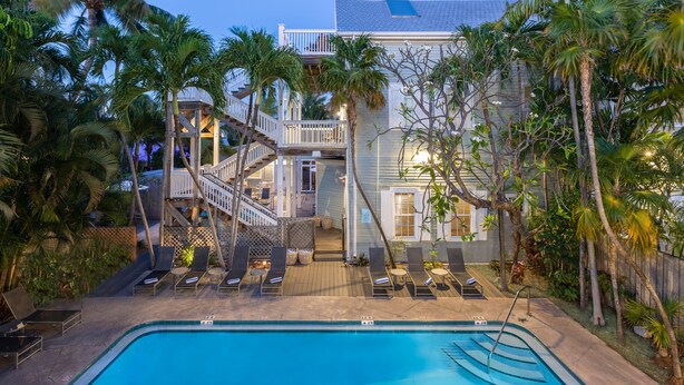 A poolside area with lounge chairs, a staircase leading to a balcony, and a pool. - The Southernmost Inn - Adults Only (Key West)