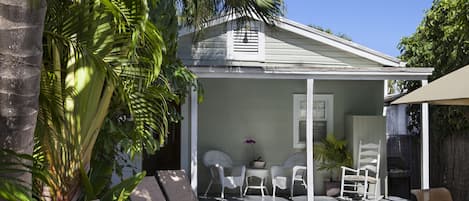 Un patio techado al aire libre con mobiliario de mimbre blanco, una mesita y una planta en maceta.