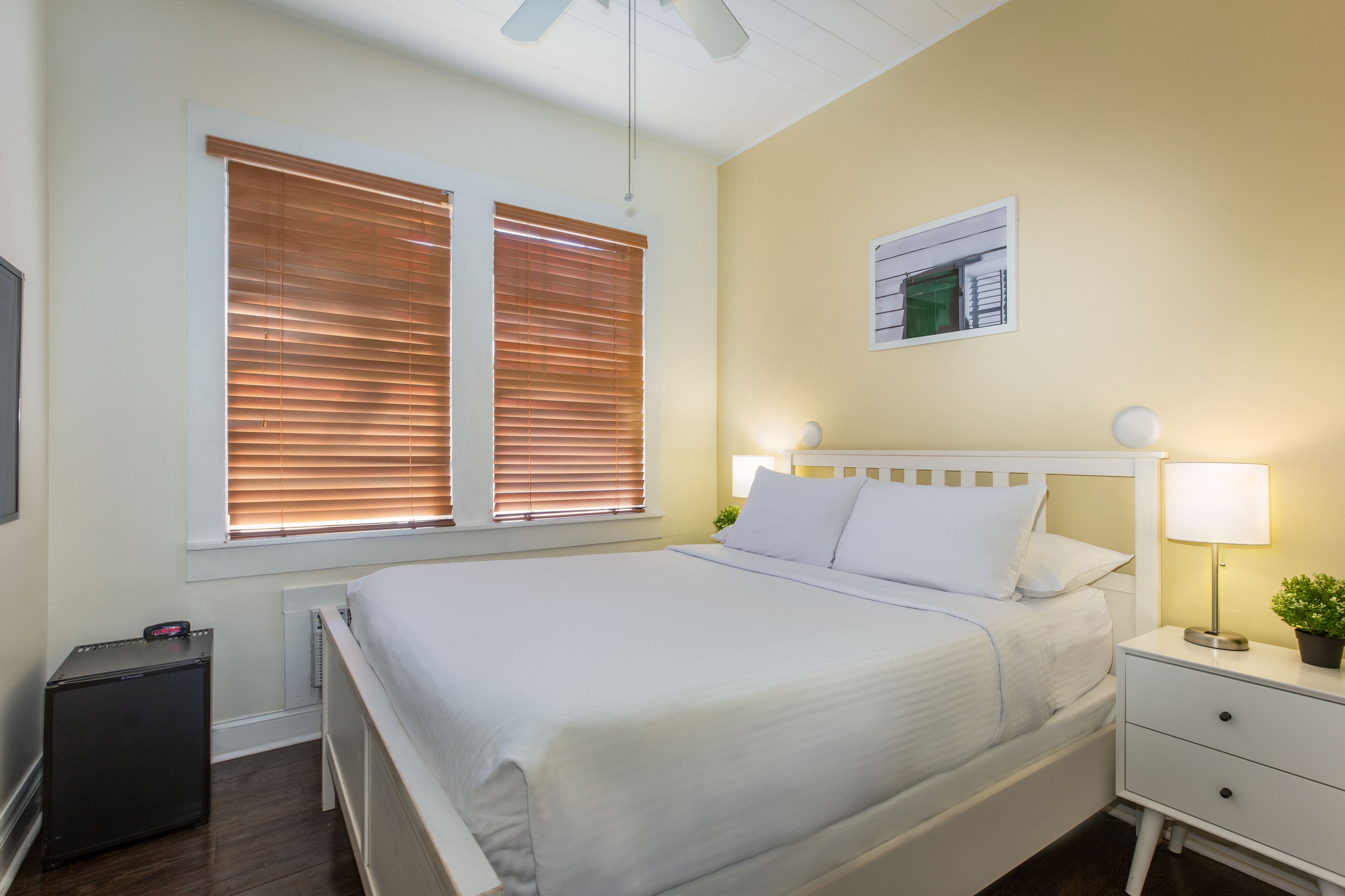 Un dormitorio ordenado con cama, mesita de noche, lámpara y un pequeño radiador.