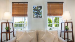 A beige sofa with two pillows, flanked by two wooden side tables with lamps and potted plants, against a white wall with a framed picture of a tree. - The Southernmost Inn - Adults Only (Key West)