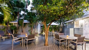 An outdoor patio with tables and chairs, surrounded by trees and a house. - The Southernmost Inn - Adults Only (Key West)