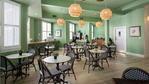 A dining area with round tables and wicker chairs, a ceiling fan, and a bar area in the background. - The Southernmost Inn - Adults Only (Key West)
