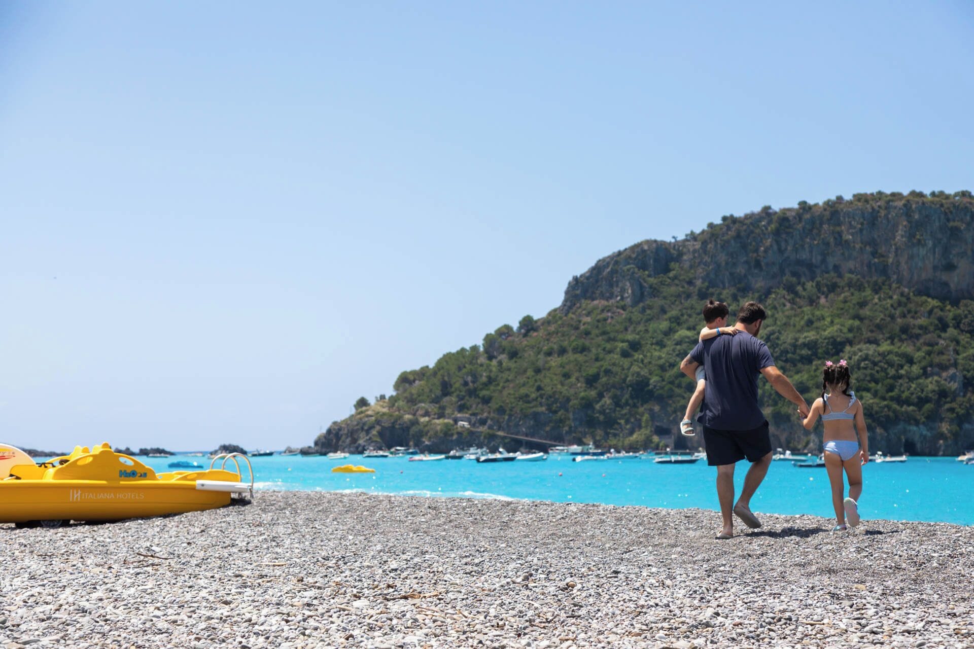 A pebbled beach with a yellow inflatable boat and a rocky hill in the background.