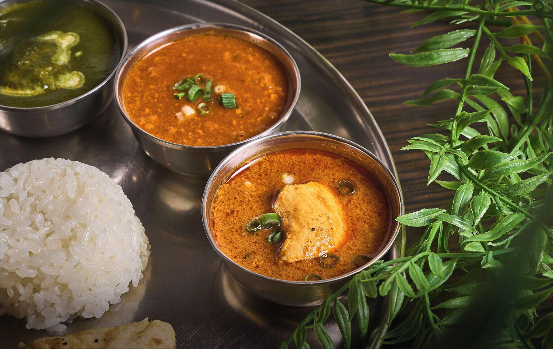 A tray with three bowls of curry, a mound of rice, and a green leafy vegetable.