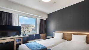 Hotelkamer met een televisie, twee bedden, een bureau en een raam met uitzicht op de stad.