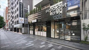 Een modern hotel met een glazen gevel, borden met 'Madras Spice' en 'Daiwa Roynet Hotel', en een voetgangersoversteek.