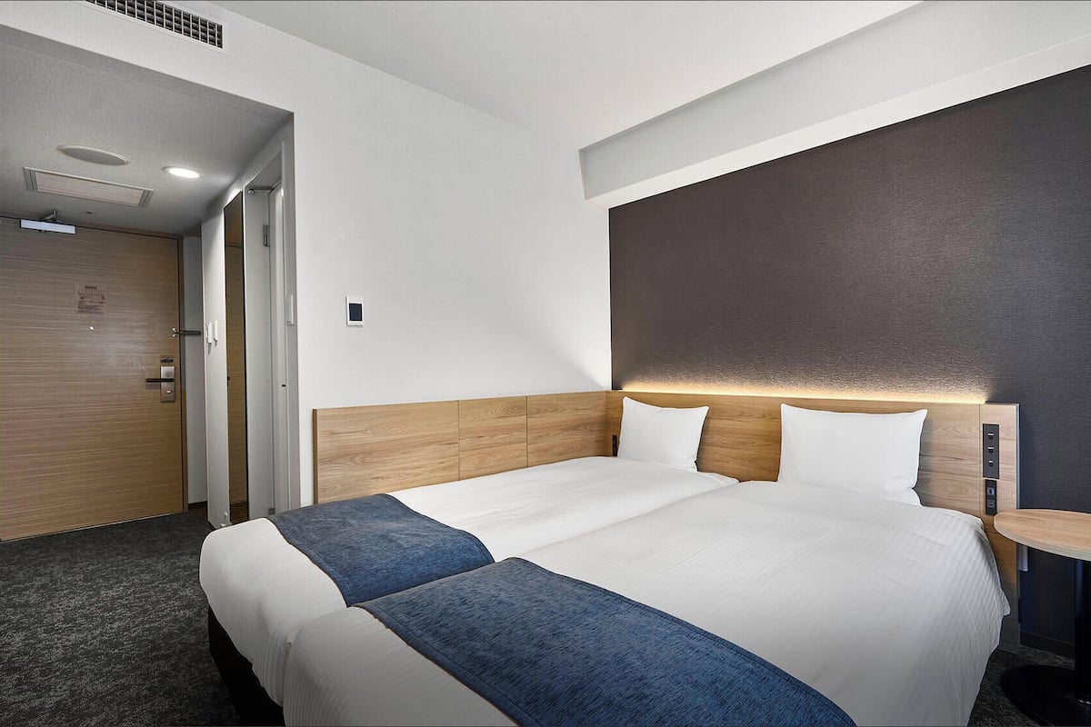 A hotel room with a large bed, a bedside table, a wall-mounted light, and a door.