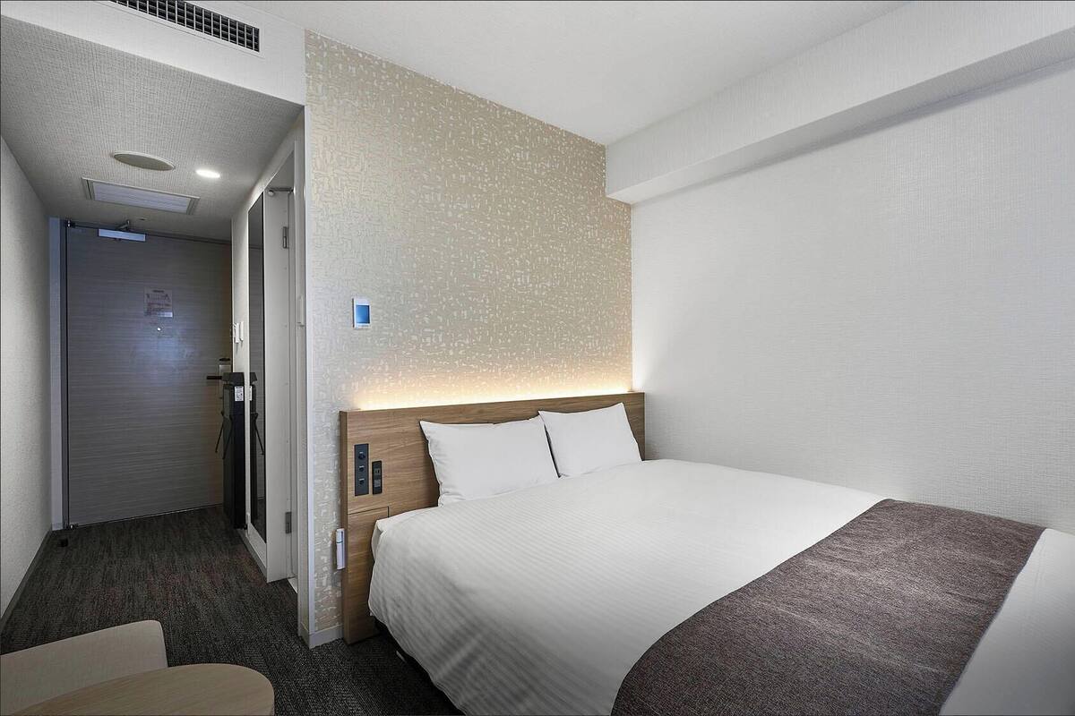 A hotel room with a bed, a desk, and a door leading to a bathroom.