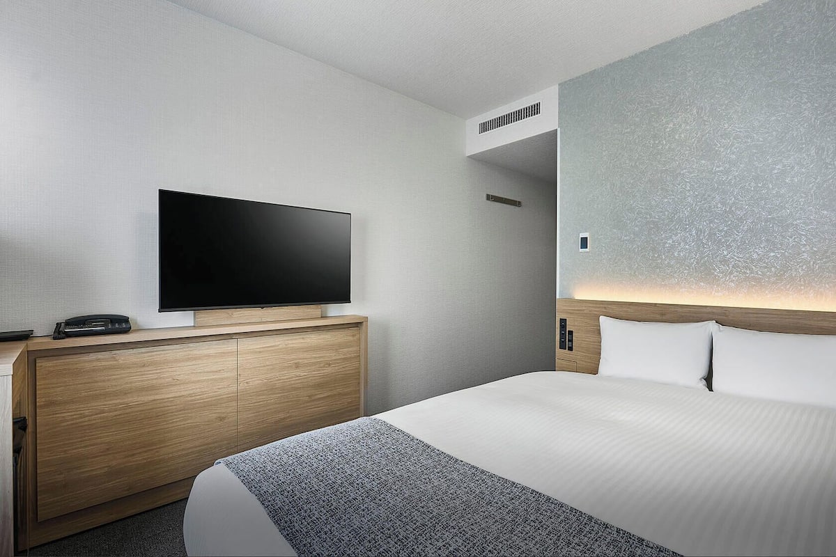 A hotel room with a bed, a TV, a wooden dresser, and a wall-mounted heater.