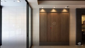 Een receptiegedeelte van een Daiwa Roynet Hotel met een modern design, met een wandpaneel van hout met het hotel logo, een glazen deur en een betegelde vloer.