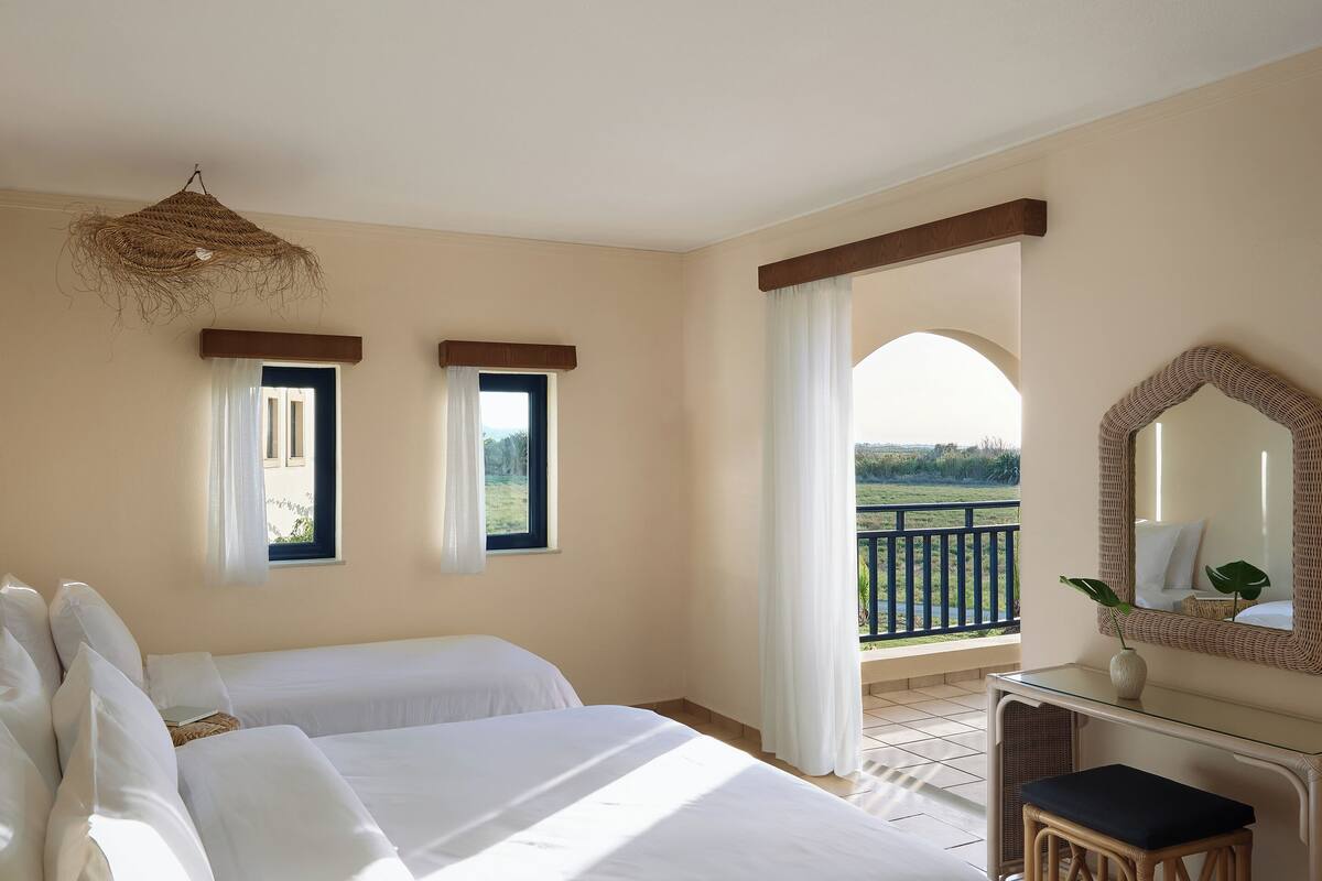 A bedroom with two beds, a balcony, a desk, and a mirror.