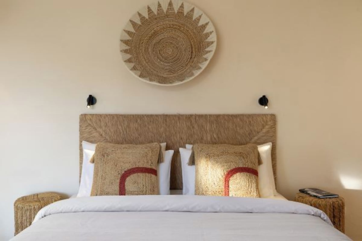 A bed with a woven headboard, two pillows with red accents, and a round wall decoration.