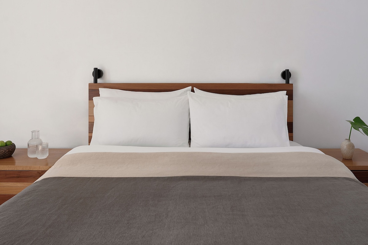 A neatly made bed with a wooden headboard, two white pillows, and a grey blanket.