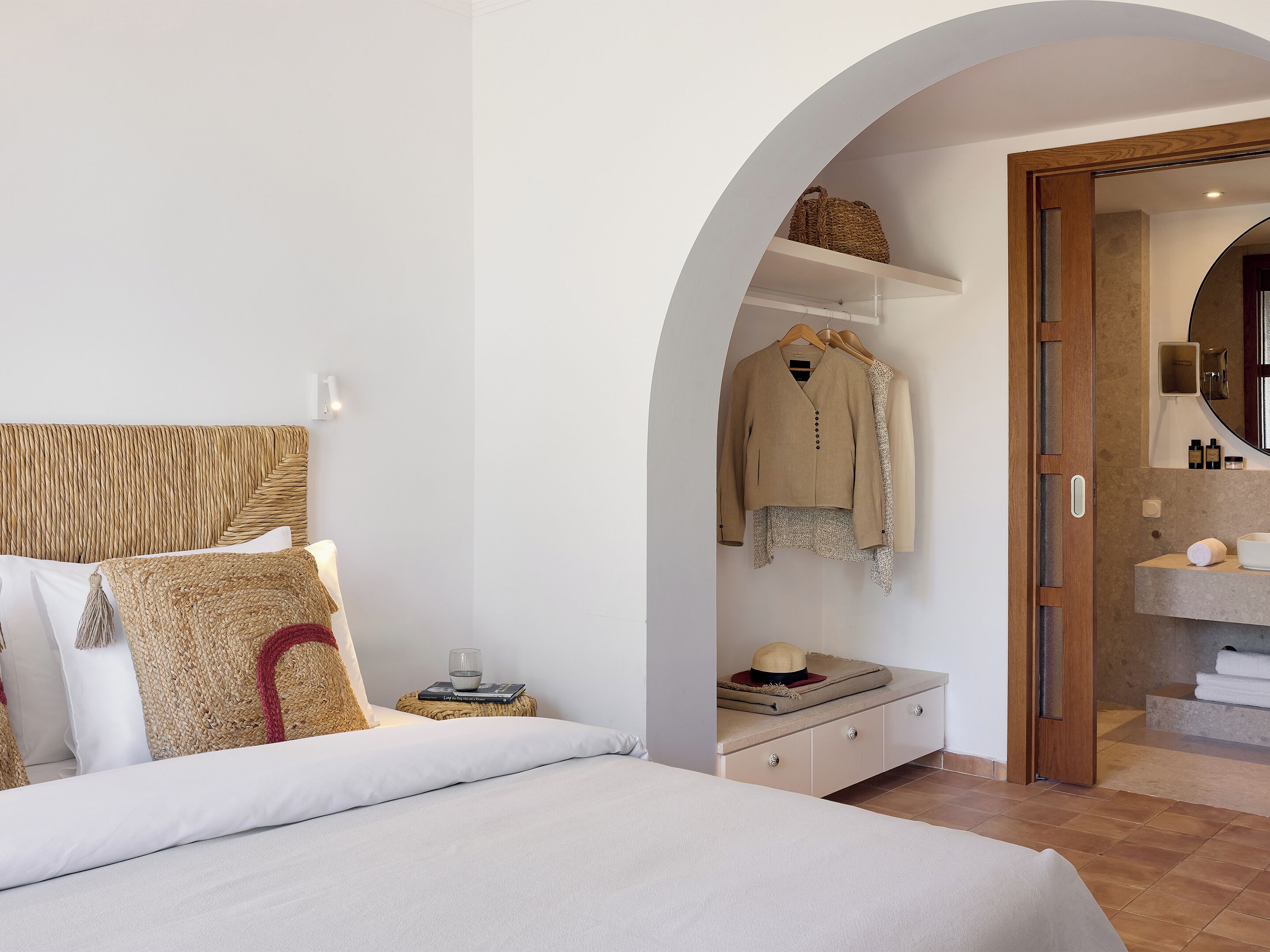 A bedroom with a bed, a wardrobe, a mirror, and a bathroom with a sink and towel.